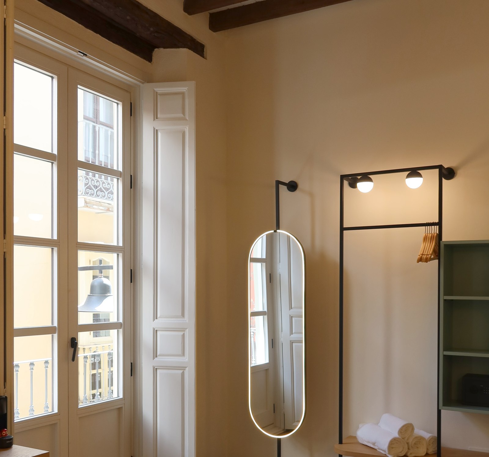 Chambre lumineuse : haute fenetre a volets sur les toits de Malaga, miroir ovale et cadre metal a lampes, Casa Beatas