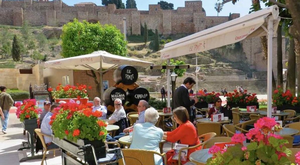 Clientes en la terraza de la bodega El Pimpi de Málaga, toneles firmados y la Alcazaba al fondo